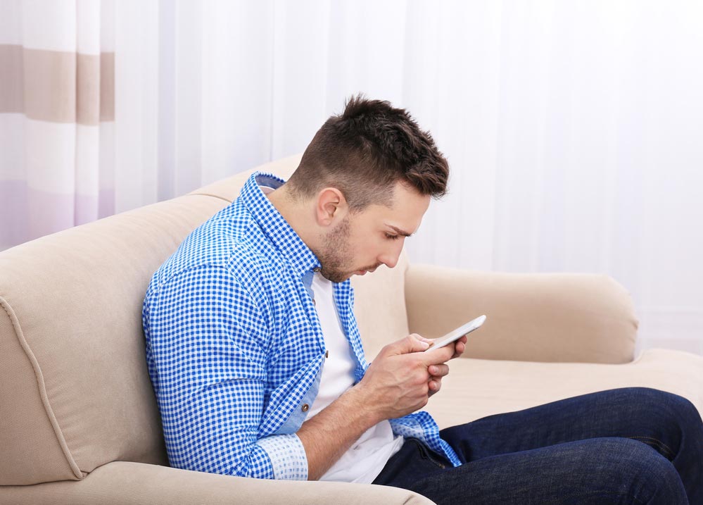 man with poor posture looking at phone on couch