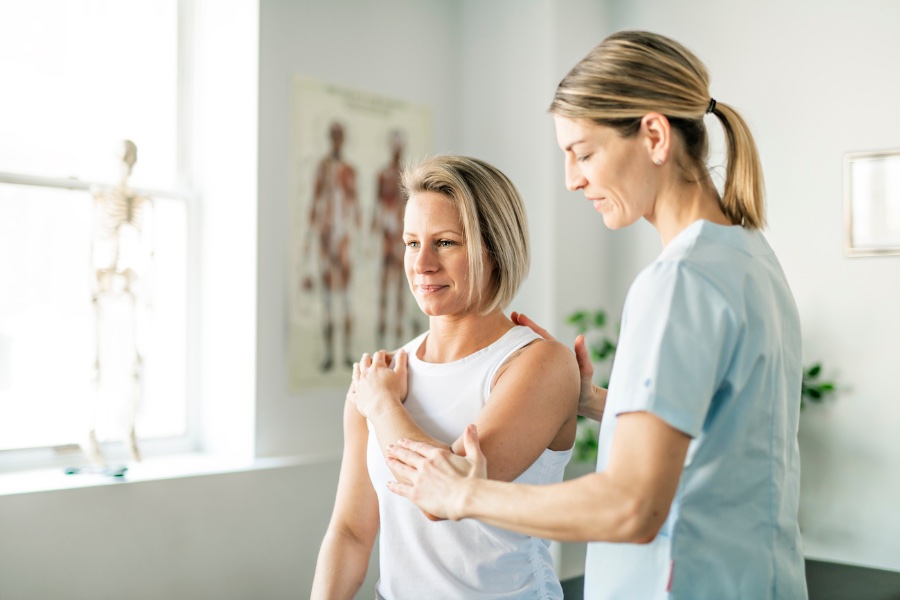 Female physiotherapist treating middle aged woman for shoulder pain